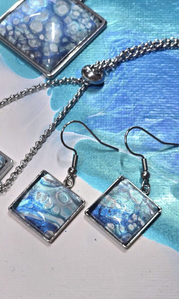 Particolare orecchini artigianali in acciaio inossidabile con cabochon quadrato 15mm tecnica fluid art color turchese, celeste azzurro iridescenti. autore AmarAnto Arte