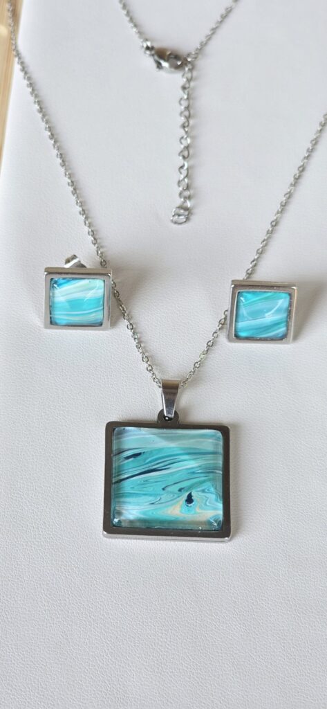 set coordinato artigianale fluid art composto da collana 45cm con cabochon quadrato 20mm e orecchini 10mm in acciaio inossidabile vernice acrilica multicolor turchese iridescente, blu, bianco. autore AmarAnto Arte