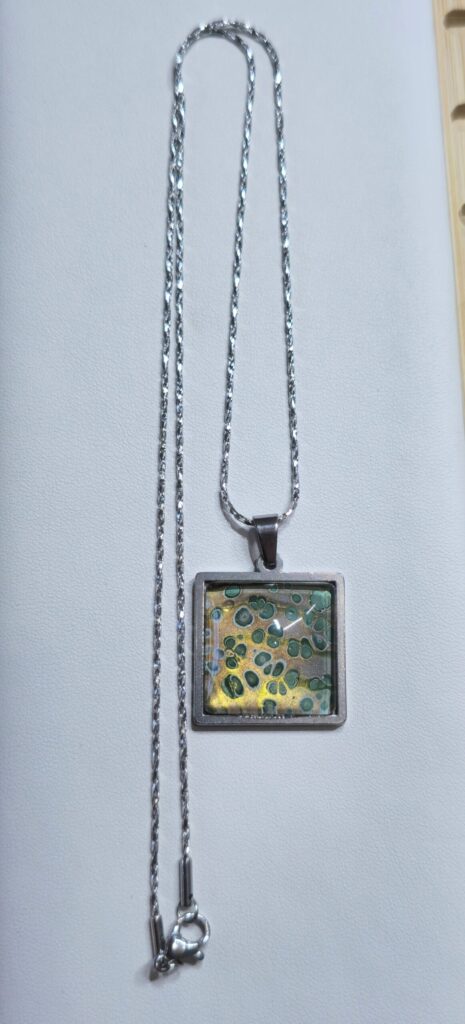 collana artigianale fluid art con ciondolo quadrato color oro e verde iridescente in acciaio inossidabile. Autore AmarAnto Arte