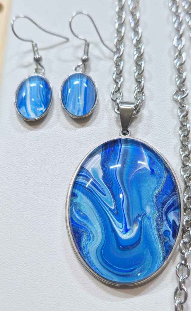 particolare collana artigianale fluid art in acciaio inossidabile lunghezza 70 cm con ciondolo ovale 30x40mm color blu, celeste, turchese iridescenti. Autore AmarAnto Arte